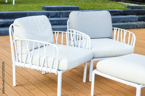 Modern outdoor seating set featuring two white metal chairs with soft cushions on a wooden deck, surrounded by green grass and stone steps in the background
