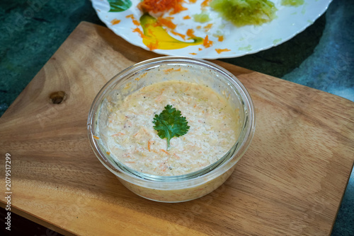Indian homemade raita with cucumber, herbs and dahi yogurt on a cutting board background. View from above. healthy cooling food concept.