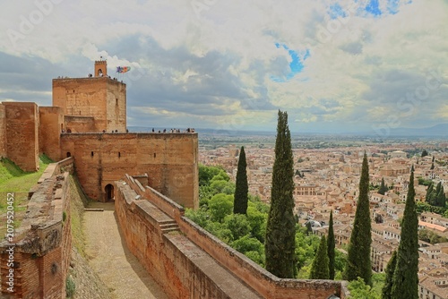 Scenic view of Granada city from the ancient ramparts of the Alhambra fortress under a dramatic cloudy sky.
