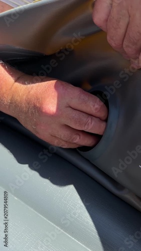 Close up of tourist hands tightening a plastic air inflation valve on an inflatable boat.
