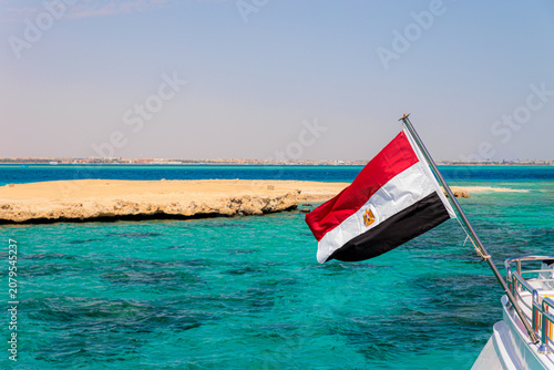 Foto Egyptian Flag Flying From a Boat Over Turquoise Red Sea Near Sandy Island Coastl