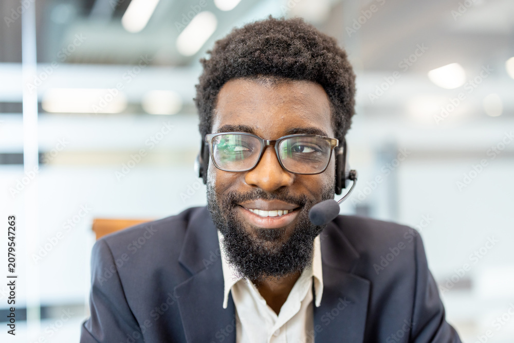 Fototapeta premium Enthusiastic service operator smiling and looking away. Wearing eyeglasses and a headset. Symbolizing friendly support. Effective communication
