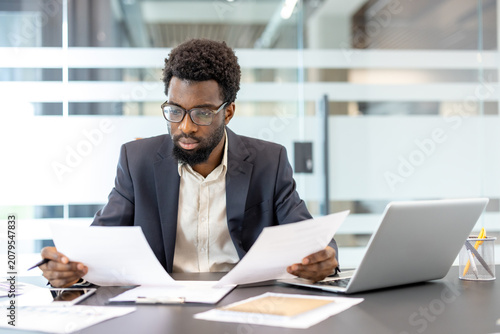 Tableau sur toile Young businessman wearing a suit and glasses sitting at a modern office desk, me