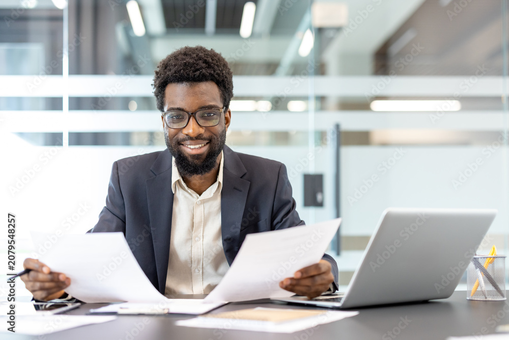 Obraz premium Confident entrepreneur sitting at his desk, holding documents, and smiling at the camera, symbolizing professionalism, success, and leadership in a contemporary workspace