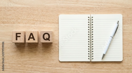 Faq letters on wooden blocks with an open spiral notebook and a pen on a desk for customer service and frequently asked questions support
