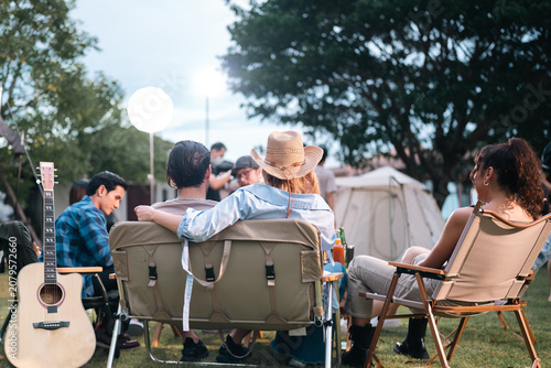 Camping friend guitar chair outdoor tent group gathering with seated adult acoustic music relaxed leisure grass campsite under tree