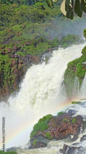 Magnificent waterfall crashing into the river below. A beautiful rainbow forms in the mist amidst the lush, green jungle landscape