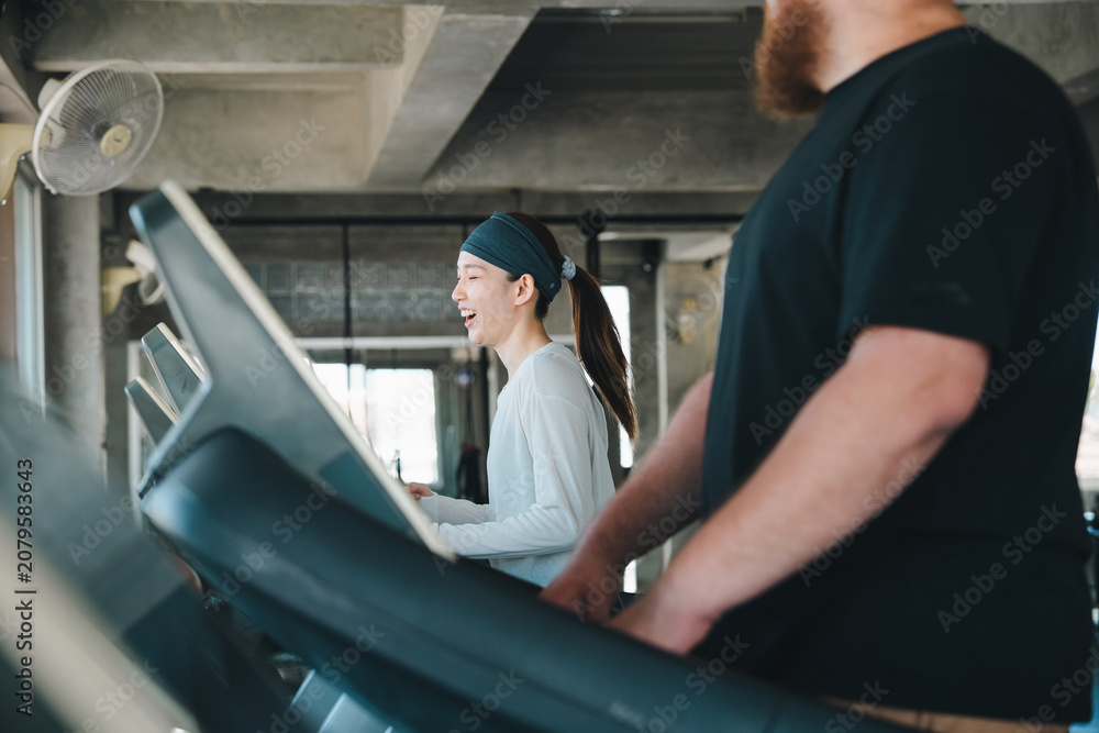 Fototapeta premium Gym treadmill woman man workout fitness exercise running training active indoor gym with smiling woman and bearded man exercising treadmill, cardio workout, healthy lifestyle, modern fitness center