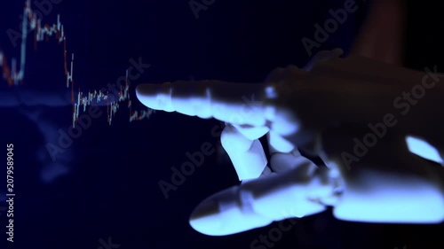 AI robot hand analyzing financial data from a computer screen. Close-up of futuristic cybernetic arm reading charts in modern office.