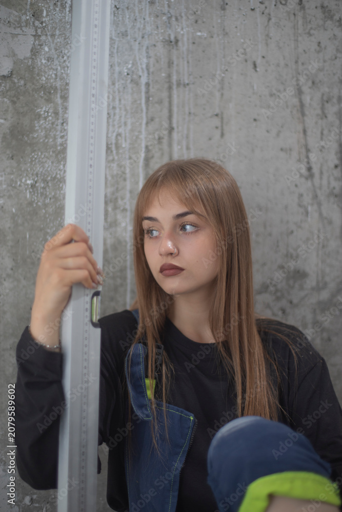 Fototapeta premium Tired female builder holding spirit level tool sitting by concrete wall with copy space