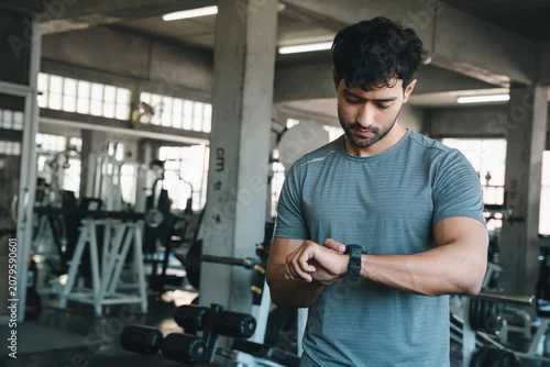 Panel kuchenny z motywem Man gym watch fitness exercise athlete checking wearable device in industrial training center with dumbbell equipment focused expression