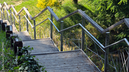 High angle view of a wooden park staircase with a geometric zigzag metal handrail descending a hillside