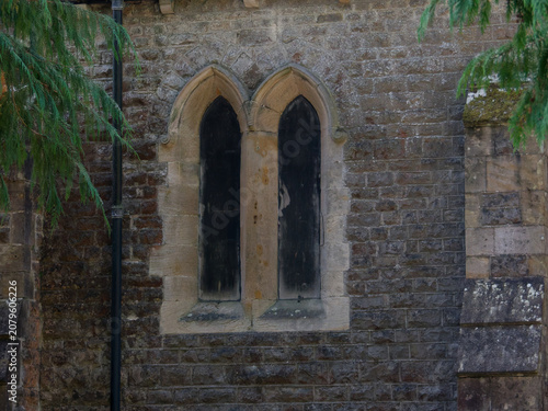 A stone wall with two arched windows, showing old weathered textures and dark glass.