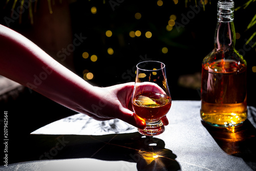 Cuadro en lienzo Hand holding glencairn glass with amber scotch whisky on dark table with bottle