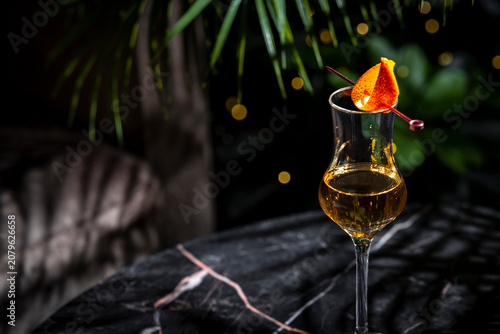 Fotografía Golden alcoholic drink cocktail in tiny grappa glass with orange peel on elegant black marble table