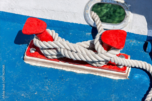 A red mooring bollard holds a thick marine rope tightly. This deck element helps secure the ship in place at the berth during day. It is an important part of safe docking.