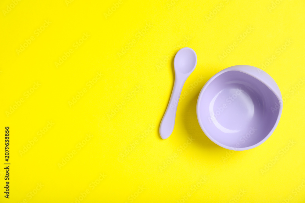 Obraz premium Baby tableware. Plastic bowl and spoon on yellow background, flat lay. Space for text