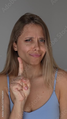 Young blonde woman shows a no-no-no gesture with her hand, expressing refusal, disagreement, warning and rejection, emphasizing strong denial and clear negative response on a grey background
