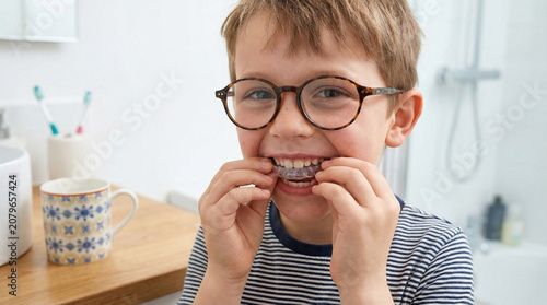 Young boy with glasses smiling while putting on clear dental aligners