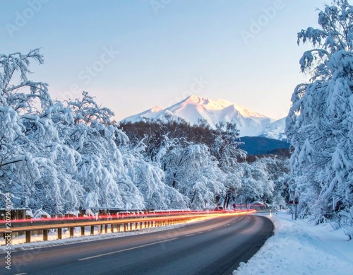 beautiful winter road with dark night road through forest and mountains, wintery scene at sunset