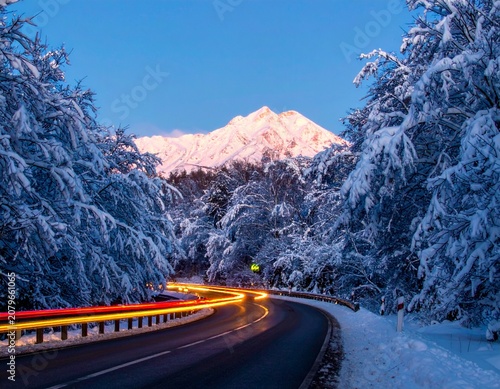 beautiful winter road with dark night road through forest and mountains, wintery scene at sunset