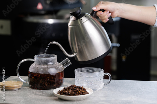 Fotografija Hand pouring boiling water from gooseneck kettle into glass teapot with loose co