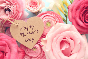 Happy Mother's Day tag in shape of heart and beautiful flowers on light blue background, flat lay