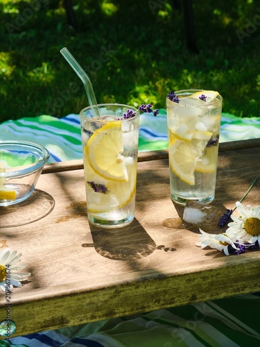 The process of preparing cold water with lemon and ice cubes in tall glasses outdoors in summer.