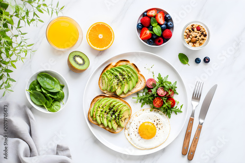 Flat lay of healthy breakfast with avocado toast, fried egg, and fresh fruits