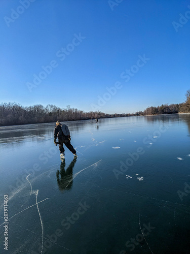 Obraz na plátne A woman wearing a backpack ice skates away down a wide expanse of smooth clear black ice on a frozen lagoon at Toronto Island under a brilliant blue sky