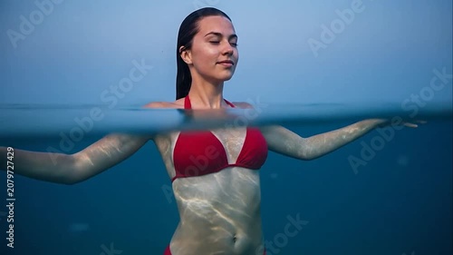 Young woman in red bikini floating peacefully in calm blue ocean water with split level view
