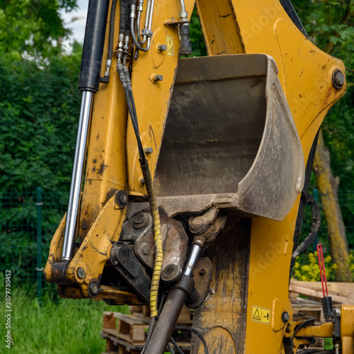 Close up of a yellow excavator bucket and hydraulic piston mechanism at a construction site