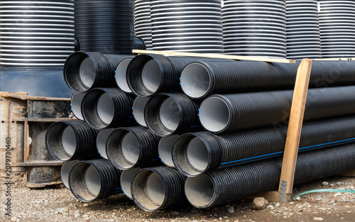 Stack of black corrugated plastic drainage pipes stored at a road construction site