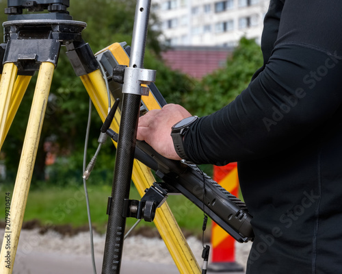 Close up of a surveyor operating a geodetic data controller mounted on a tripod at a construction site