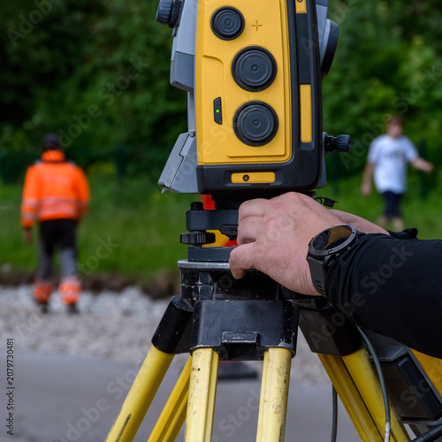 Close up of a total station geodetic instrument on a tripod with a surveyor hand adjusting the device at a construction site
