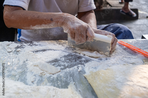 Obraz na plátne A street food vendor preparing cakwe (you tiao) dough with a metal bench scraper on a floured worktable at a traditional market in Central Java, Indonesia