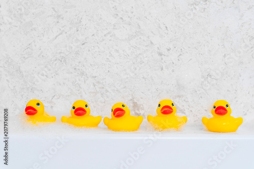Fotografie Row of five cheerful yellow rubber ducks lined up along the white edge of a bathtub in a playful bath scene