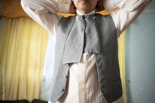 Konstfotografi Unrecognizable groom fastening his traditional silver cravat tie around high col