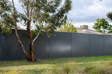 A boundary wall beside eucalyptus tree separating retail and residential area in Australia. Barriers for amenity protection. House roofline behind the fence.