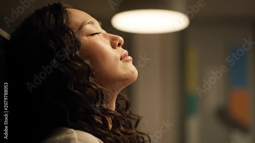 Young woman with closed eyes enjoying a moment of peace and relaxation under soft indoor lighting.