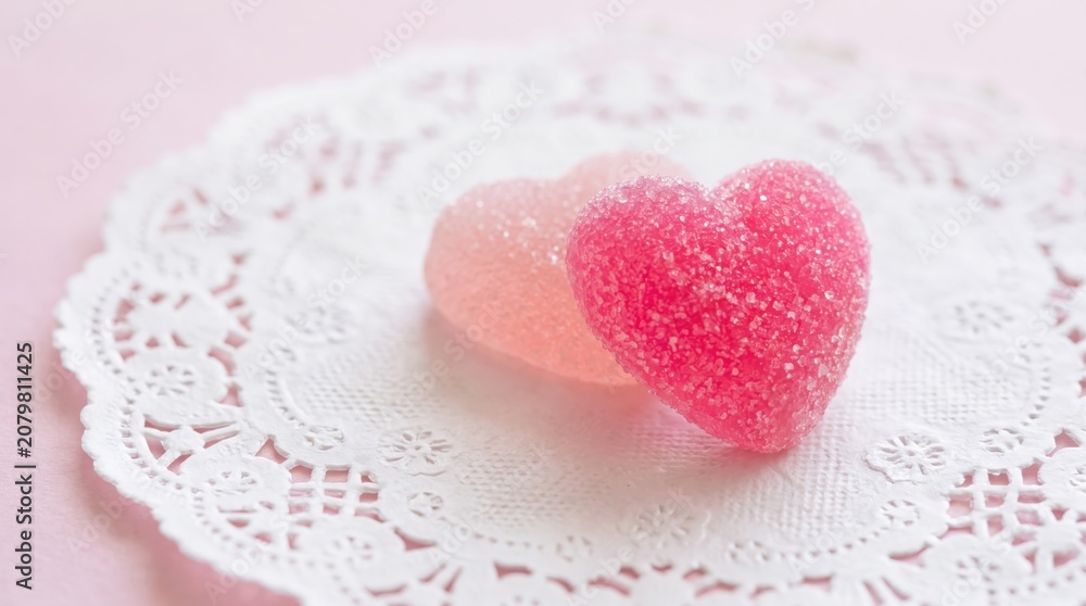 Obraz premium Two heart-shaped candies are placed on a white doily atop a pink surface with lace details.