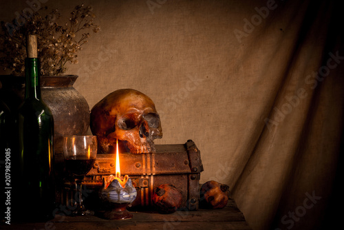 Human skull and candle with on wooden floor and old dirty wall background, and vase flower,and glass,and bottle of wine, still life concep