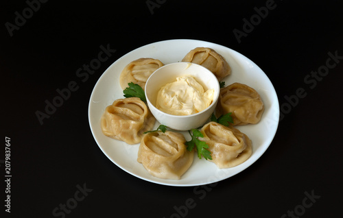 Steamed dumplings with parsley and a cup of sour cream in a round plate against a black background.
