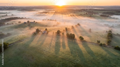 Aerial view of misty countryside with long tree shadows at sunrise