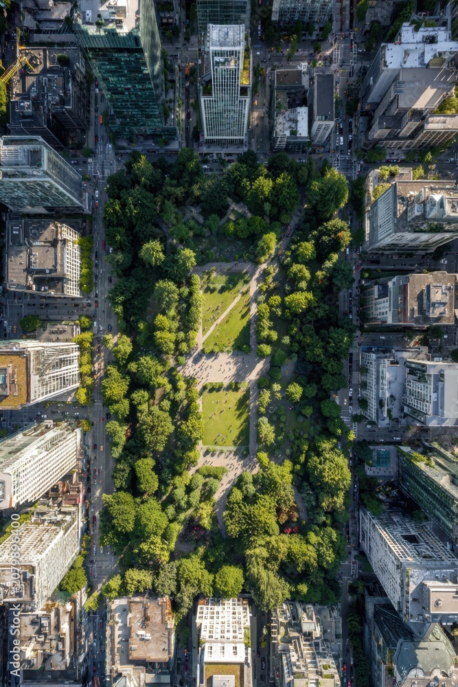 Fototapeta premium Drone shot shows a city park with green space and surrounding buildings during daytime showcasing outdoor activity and nature within an urban area in a busy city landscape