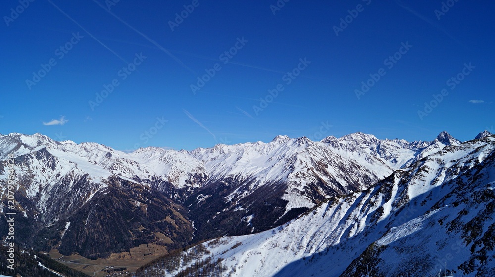 Fototapeta premium Panoramic view of snowy alpine mountain range under blue sky 