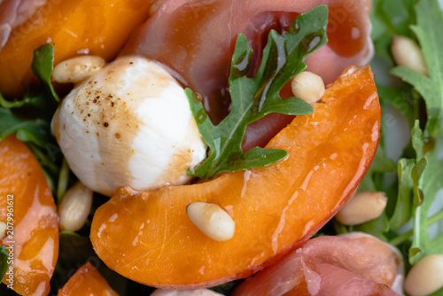Tableau sur toile Macro close-up of a fresh summer salad featuring juicy apricot slices, creamy mozzarella pearls, delicate prosciutto, peppery arugula, and toasted pine nuts