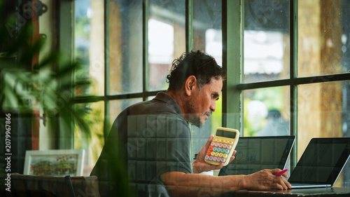 Mature businessman analyzing financial data using a calculator while reviewing reports on a laptop in a modern workspce