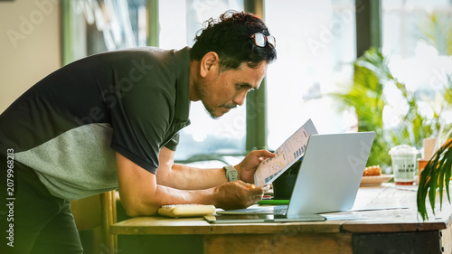 Senior businessman reviewing business reports while working on a laptop in a modern workspace. Mature entrepreneur analyzing documents