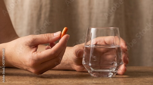 A person's hands holding an orange capsule and a glass of water, ready to take medication.